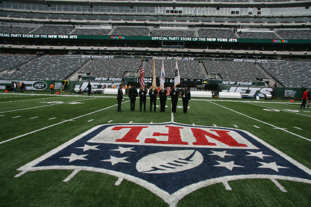 Honor Guard poses by NFL logo on Jets field. 